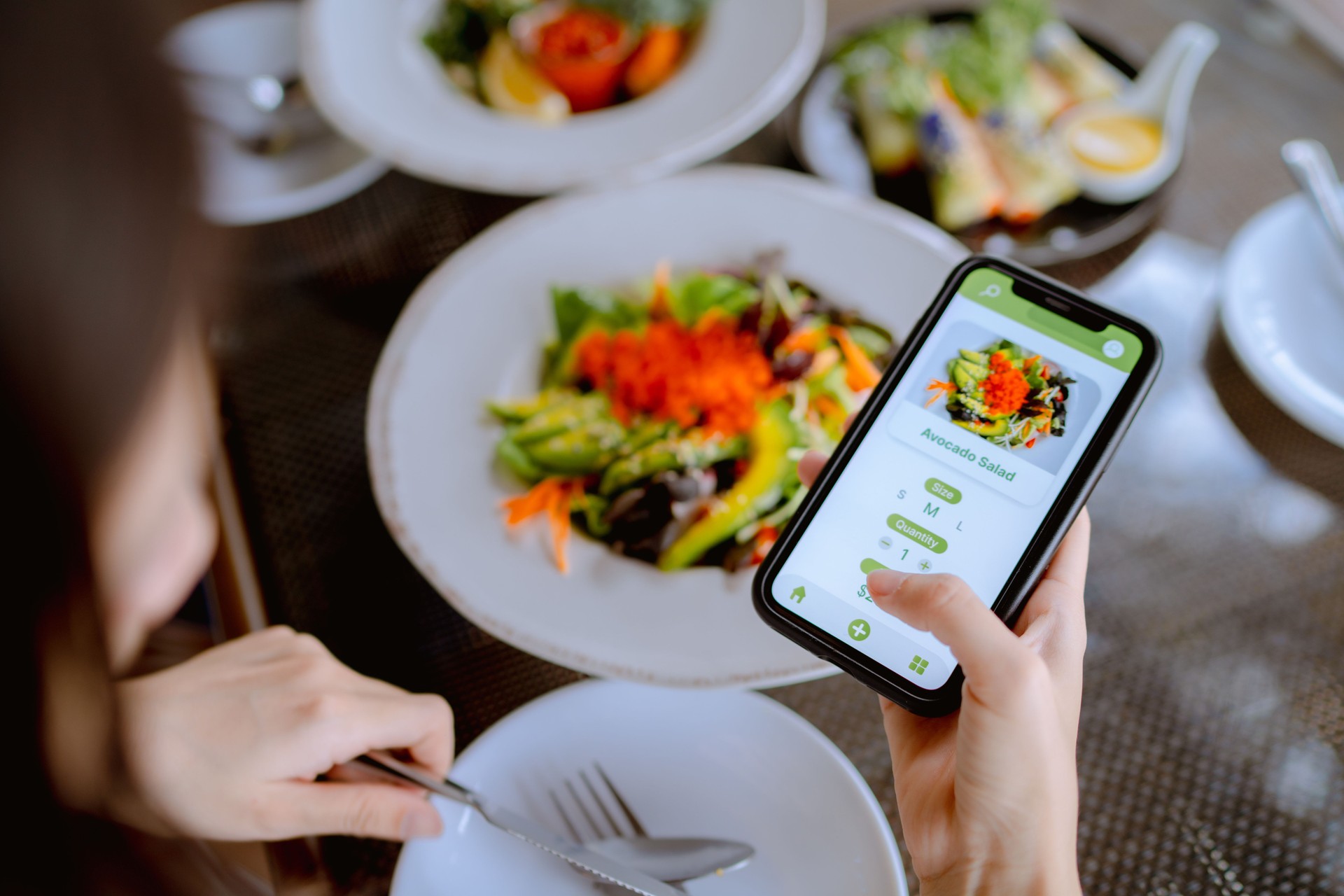 Technology makes life so much easier for young Asian woman using mobile app device on smartphone to place a food order in a restaurant.